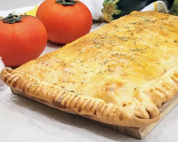 Empanada de pisto dorada y crujiente, con tomates frescos y ajo al lado. ¡Un manjar casero!