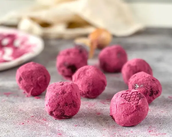 Deliciosas trufas de chocolate cubiertas de polvo rosa vibrante, algunas con un patrón grabado.