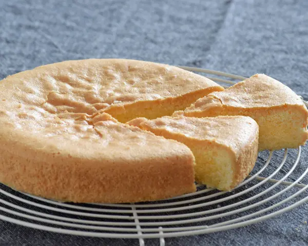 Un esponjoso bizcocho sin gluten, recién horneado y cortado en porciones, descansa sobre una rejilla.