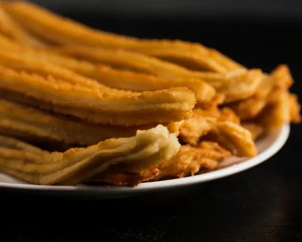 Montón de churros de patata dorados y crujientes apilados en un plato blanco.