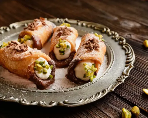 Cuatro cannoli siciliano, crujientes y rellenos de crema dulce, espolvoreados con pistachos y virutas de chocolate.