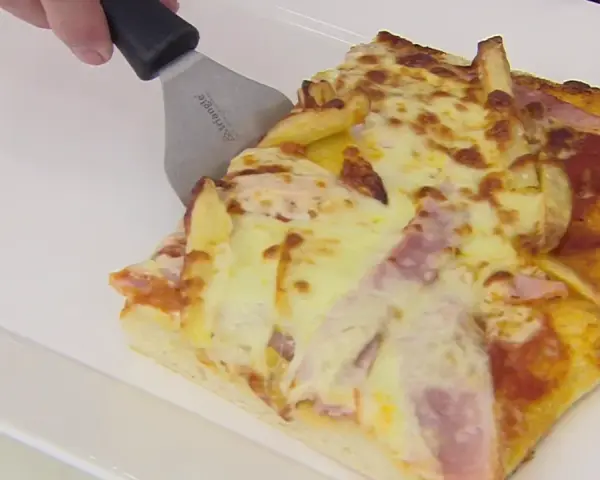 Una rebanada de pan pizza con papas fritas y jamón, lista para ser servida.
