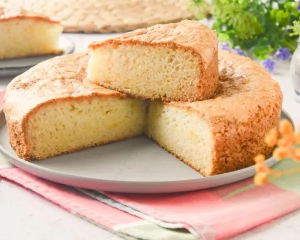 Bizcocho sin huevo esponjoso y dorado, cortado en porciones sobre un plato gris. Ideal para desayunos o meriendas.