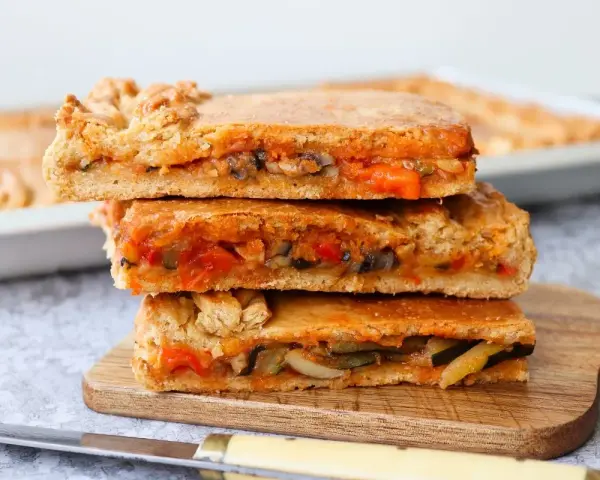Tres porciones de empanada de verduras apiladas, mostrando el relleno de pimientos, calabacín y tomate.