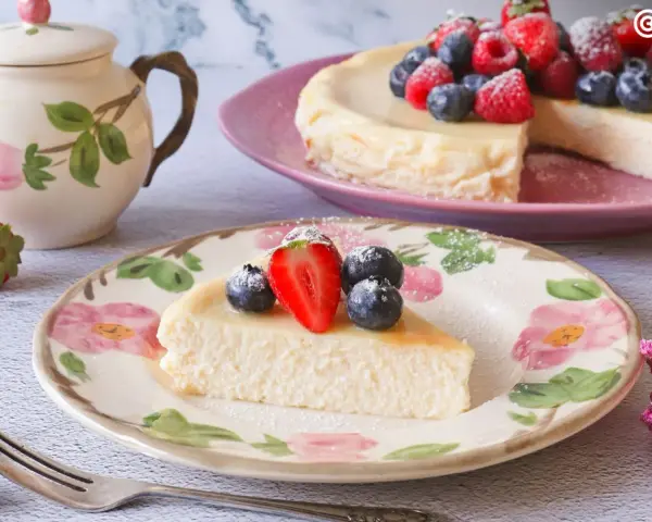 Deliciosa tarta de requesón, decorada con fresas y arándanos, servida en un plato floral.