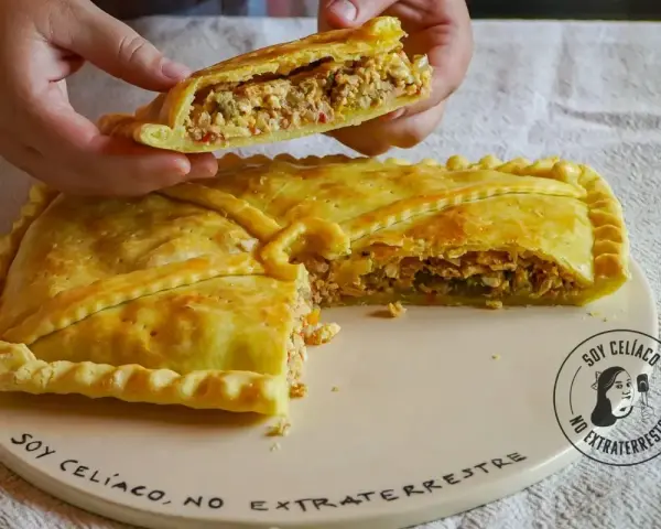 Una mano levanta un trozo de empanada de carne dorada y rellena. La masa crujiente envuelve un sabroso guiso.