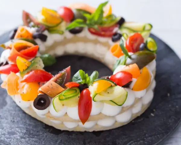 Deliciosa cream tart circular adornada con tomates, pepino, aceitunas y albahaca.