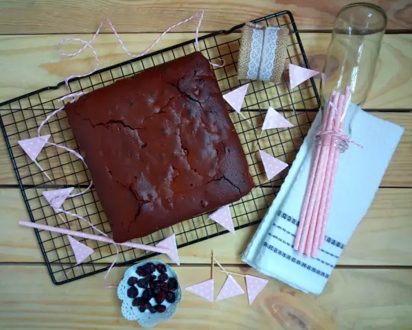 Un delicioso brownie recién horneado, listo para ser cortado. Decorado con banderines rosas y arándanos.