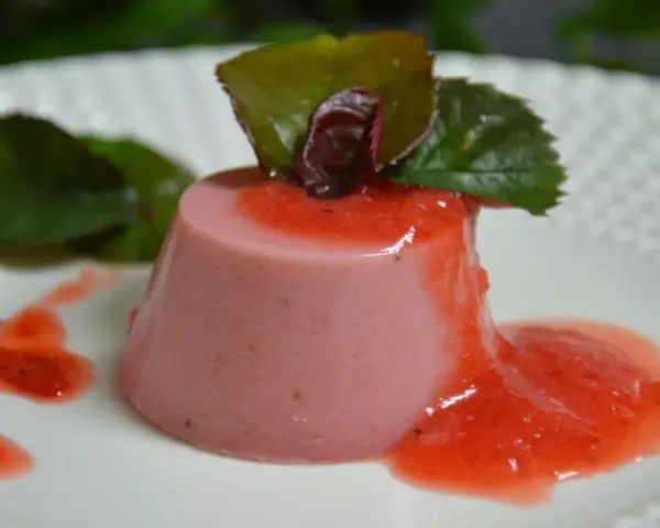 Delicioso panna cotta de fresa, bañado en salsa de fresa y decorado con hojas verdes.