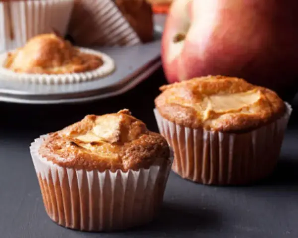Dos deliciosos muffins de manzana recién horneados, con una manzana roja al fondo.