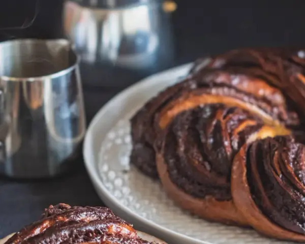 Deliciosa trenza de chocolate recién horneada, humeante junto a una taza de café.