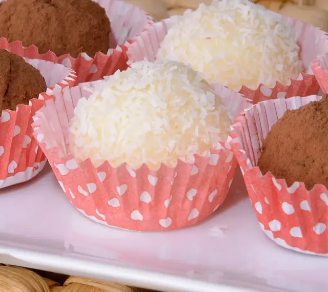 Deliciosas trufas de coco y chocolate, algunas cubiertas de coco rallado y otras de cacao en polvo, presentadas en capacillos rojos con puntos blancos.
