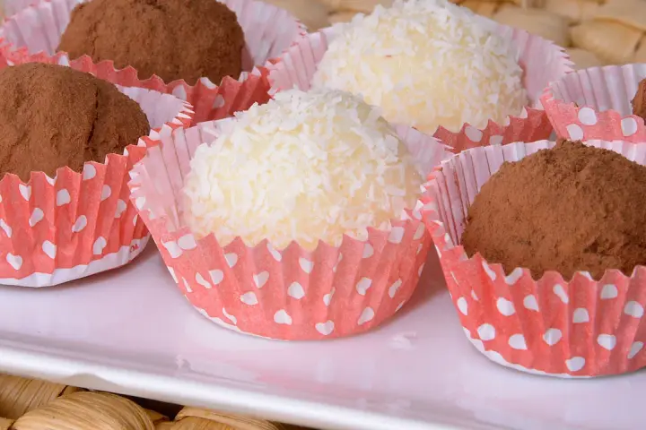 Deliciosas trufas de coco y chocolate, algunas cubiertas de coco rallado y otras de cacao en polvo, presentadas en capacillos rojos con puntos blancos.