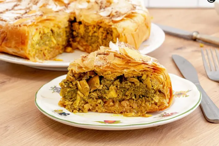 Pastela marroqui, un pastel salado de hojaldre relleno de pollo y especias, servido en un plato decorado.