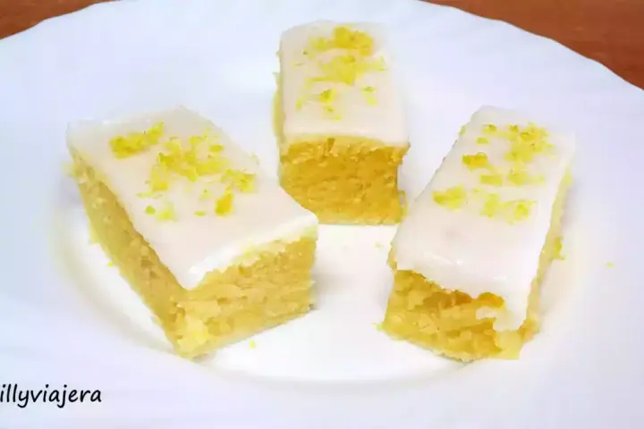 Tres porciones de brownie de limón con glaseado blanco y ralladura de limón, servidas en un plato blanco.