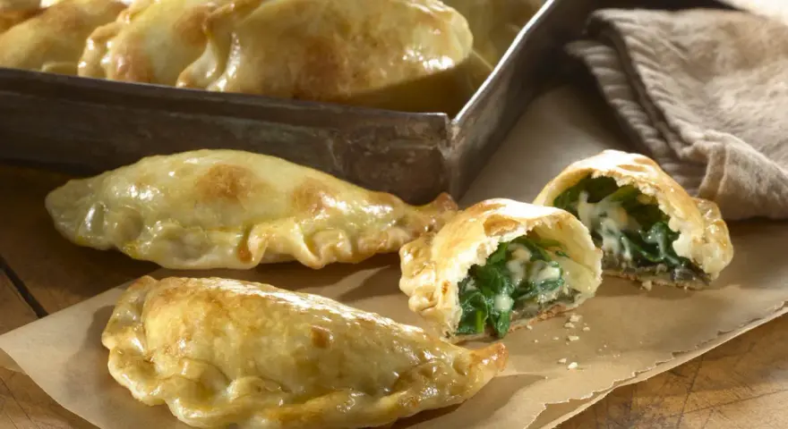 Empanadillas de espinacas y queso recién horneadas, doradas y crujientes, con un relleno cremoso y sabroso.