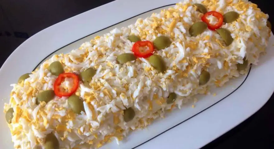 Brazo de gitano de patata cubierto de huevo duro rallado, aceitunas verdes y rodajas de pimiento rojo.