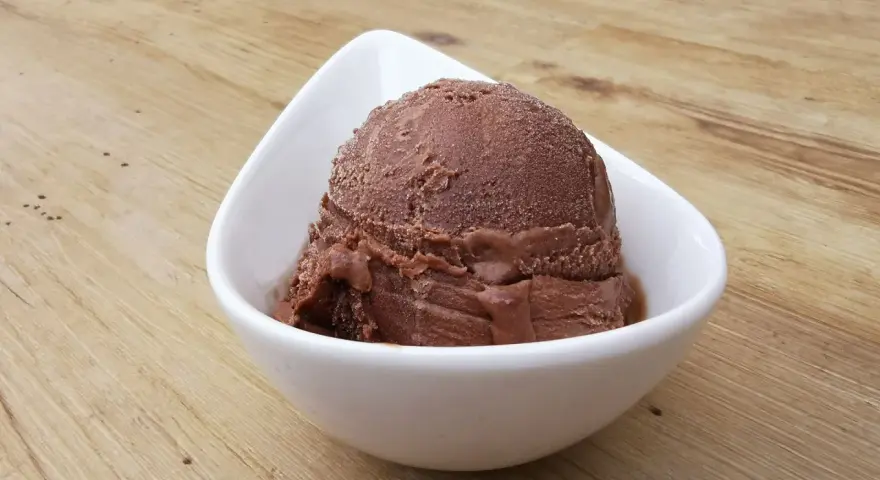 Cremoso helado de platano y chocolate en un cuenco blanco sobre una mesa de madera.