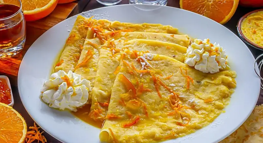 Crepes Suzette, cubiertos con ralladura de naranja y servidos con crema batida.