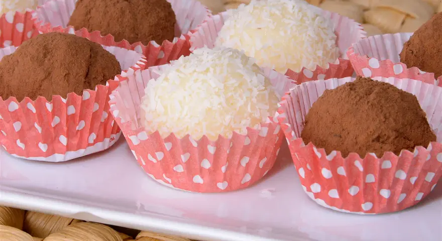 Deliciosas trufas de coco y chocolate, algunas cubiertas de coco rallado y otras de cacao en polvo, presentadas en capacillos rojos con puntos blancos.