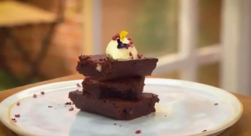 Delicioso brownie airfryer apilado, coronado con helado y pétalos.