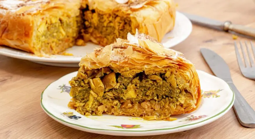 Pastela marroqui, un pastel salado de hojaldre relleno de pollo y especias, servido en un plato decorado.
