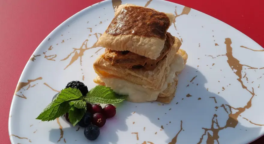 Delicioso postre de milhojas de crema, con capas crujientes y relleno dulce, acompañado de frutos rojos y menta fresca.