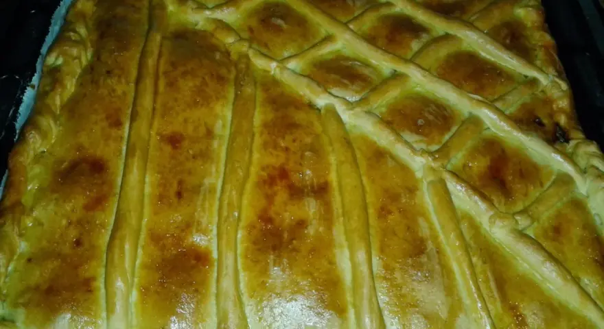 Empanada marinera dorada y crujiente, lista para disfrutar. Su masa cubierta con un enrejado perfecto promete un sabor delicioso.