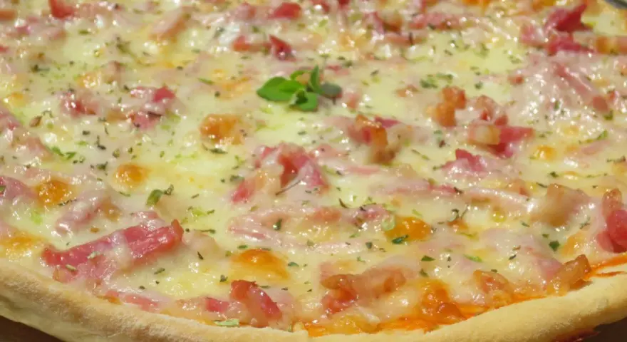 Pizza con masa hecha en Thermomix, cubierta de queso fundido, trocitos de bacon y hierbas aromáticas.