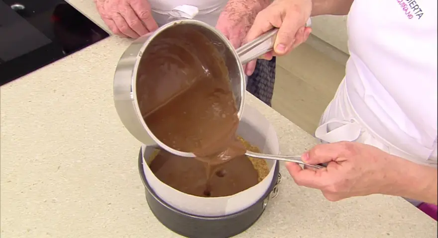 Vertiendo cobertura de chocolate sobre una base de galleta para un delicioso pastel de chocolate.