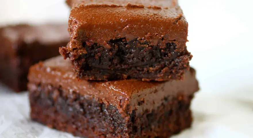 Dos deliciosos brownies con nueces apilados, cubiertos con glaseado de chocolate cremoso.