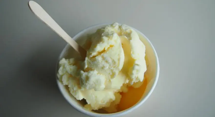 Un cremoso helado de melón en un cuenco blanco, listo para ser disfrutado con su cuchara de madera.