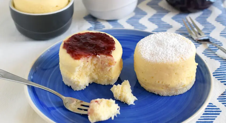 Dos bizcochos de microondas en un plato azul. Uno tiene mermelada de fresa y el otro azúcar glas.
