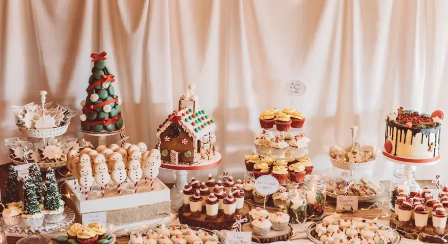 Mesa llena de postres navideños: árbol de macarons, casa de jengibre, muñecos de nieve, cupcakes y galletas.