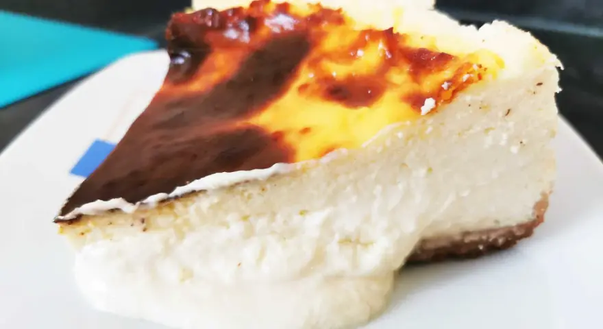 Porción de chese cake con borde quemado y relleno cremoso, servida en plato blanco.