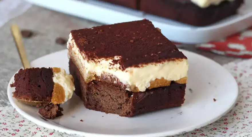 Un trozo de brownie de chocolate con una capa cremosa y espolvoreado de cacao. ¡Un delicioso brownie chocolate blanco!