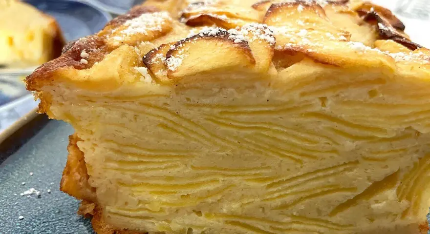 Un trozo de pastel de capas con trozos de manzana en la parte superior, espolvoreado con azúcar glas. Un postre invisible aux pommes.