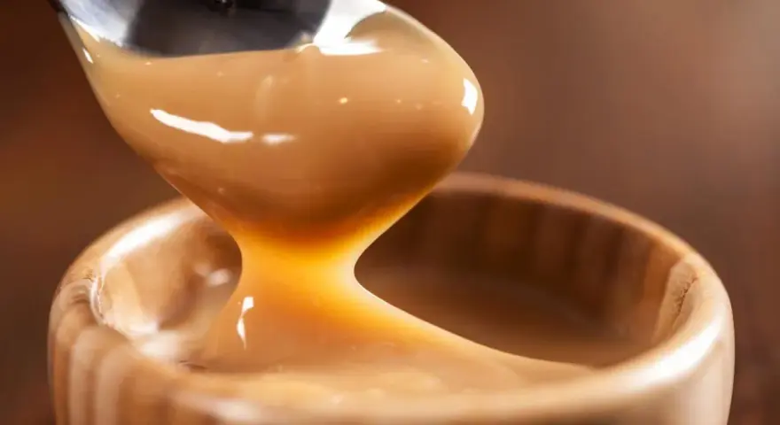 Cuchara vertiendo manjar blanco cremoso en un cuenco de madera.