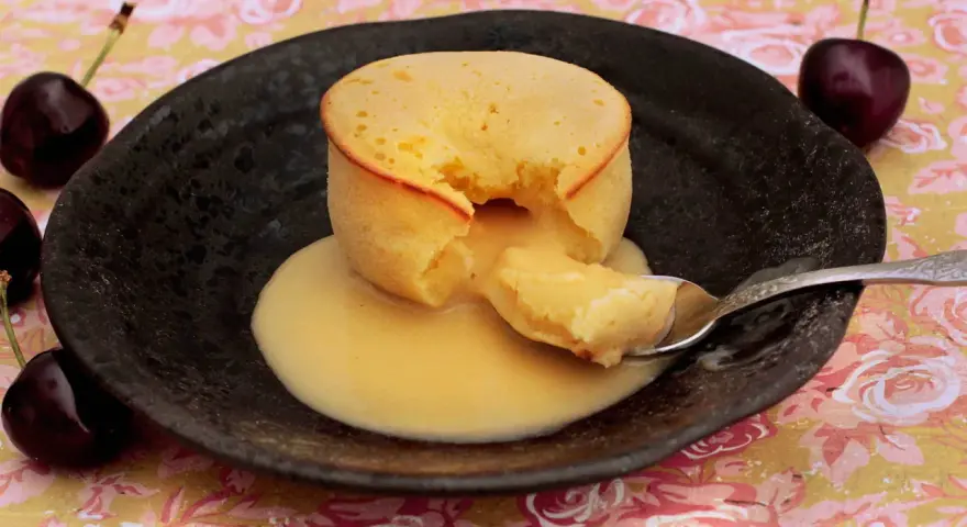 Coulant de chocolate blanco con interior cremoso, servido en plato negro con cerezas.