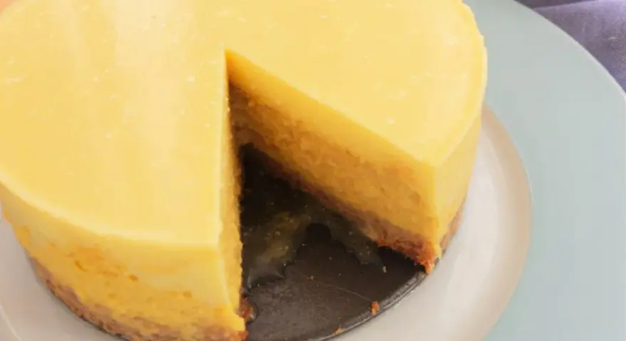 Tarta mango cremosa, con una porción retirada, sobre plato azul claro.