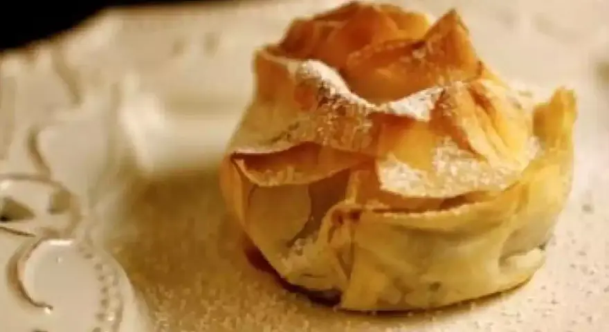 Delicioso saquito de pasta filo relleno de queso, espolvoreado con azúcar glas sobre un plato blanco.