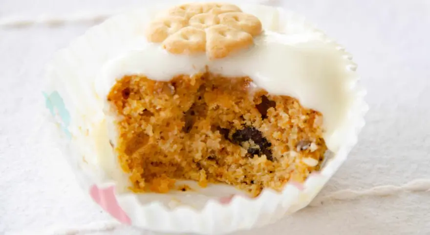 Un muffin de zanahoria con glaseado blanco y una galleta decorativa en forma de flor.