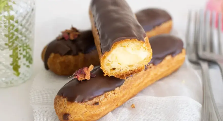 Pastel eclair cubierto de chocolate, relleno de crema. Decorado con pétalos secos.