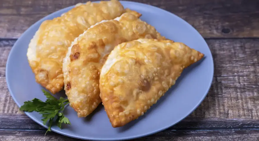 Tres empanadas doradas y crujientes, perfectas para tus recetas con obleas de empanadillas. Decoradas con perejil fresco.