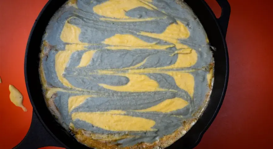 Pastel de maíz con remolinos grises y amarillos en una sartén de hierro fundido.