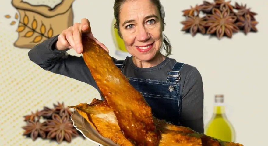 Mujer sonriente muestra una coca de vidre dorada, con ingredientes como harina, anís y aceite de oliva de fondo.