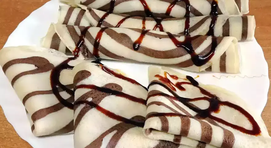 Deliciosos crepes de chocolate rayados, enrollados y doblados, cubiertos con sirope de chocolate.