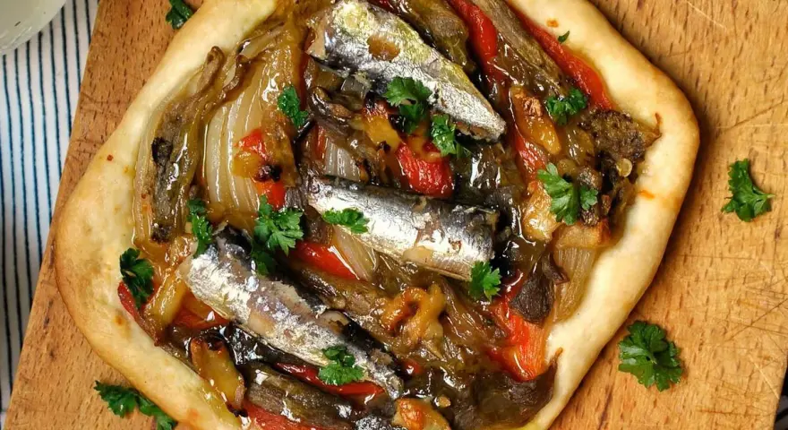 Coca de recapte con verduras asadas y sardinas, decorada con perejil fresco.