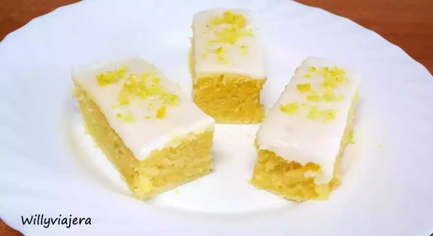 Tres porciones de brownie de limón con glaseado blanco y ralladura de limón, servidas en un plato blanco.