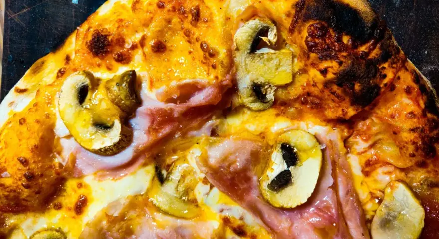 Pizza masa madre con champiñones y jamón, con bordes dorados y burbujas de queso fundido.